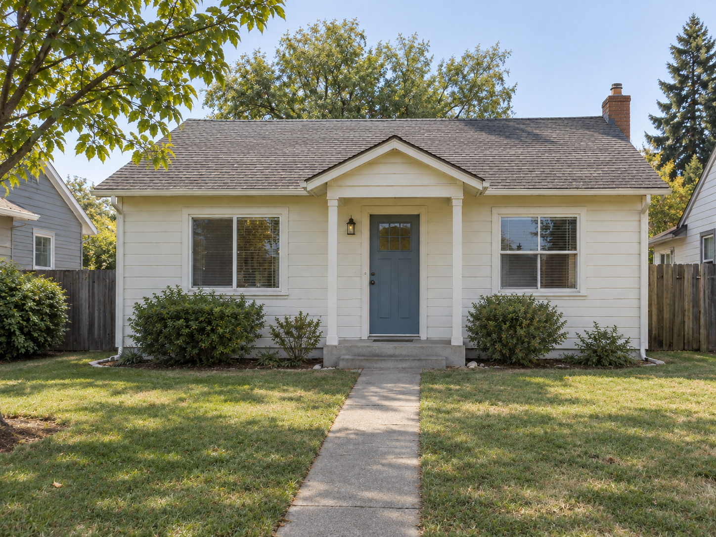 A modest white home with a blue front door and a lived-in front yard